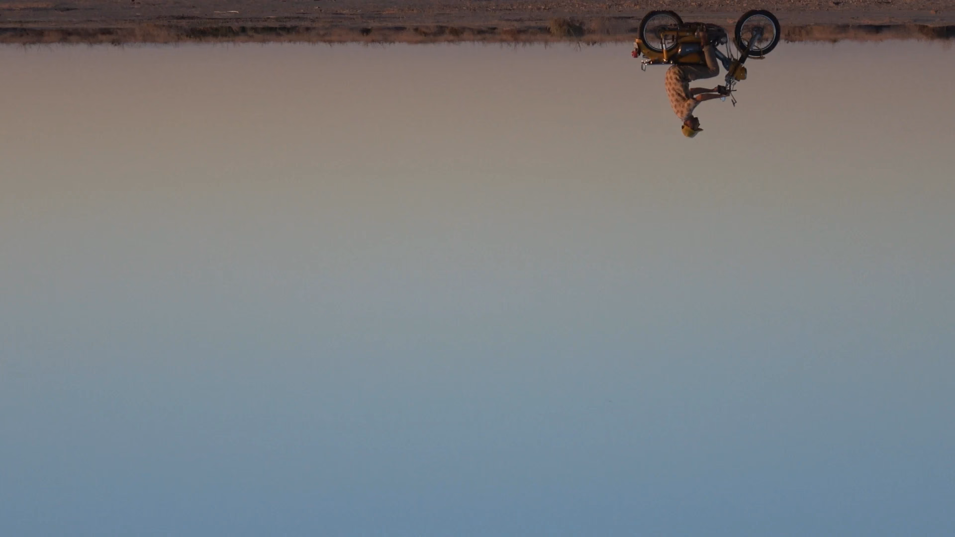An inverted desert scene with a motorcycle suspended overhead